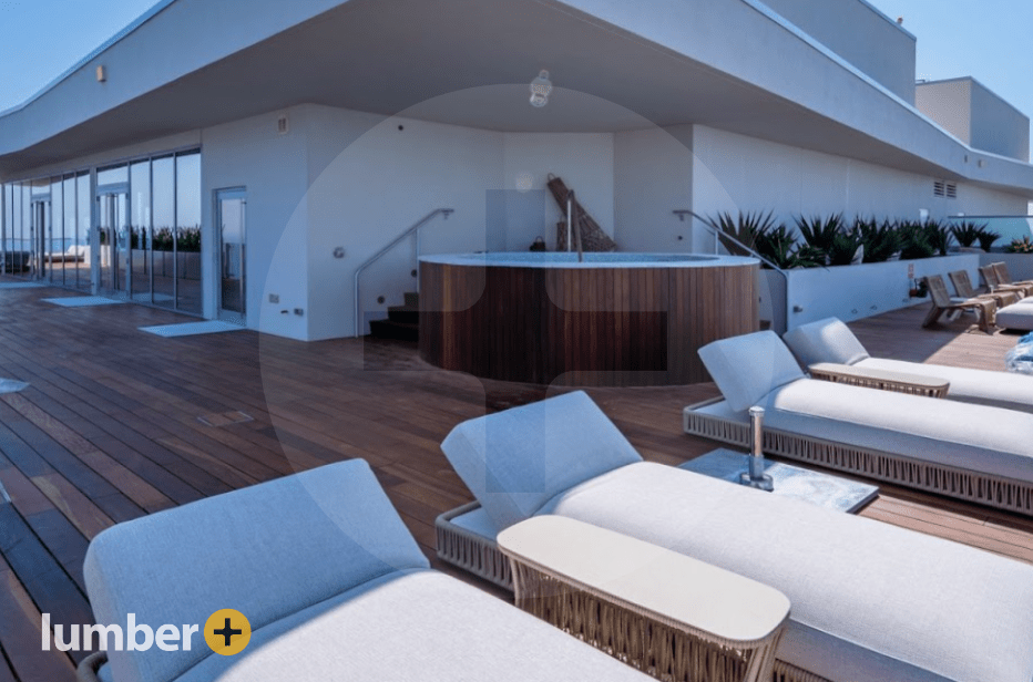 Wooden pool deck with lounge chairs next to a hot tub and swimming pool.