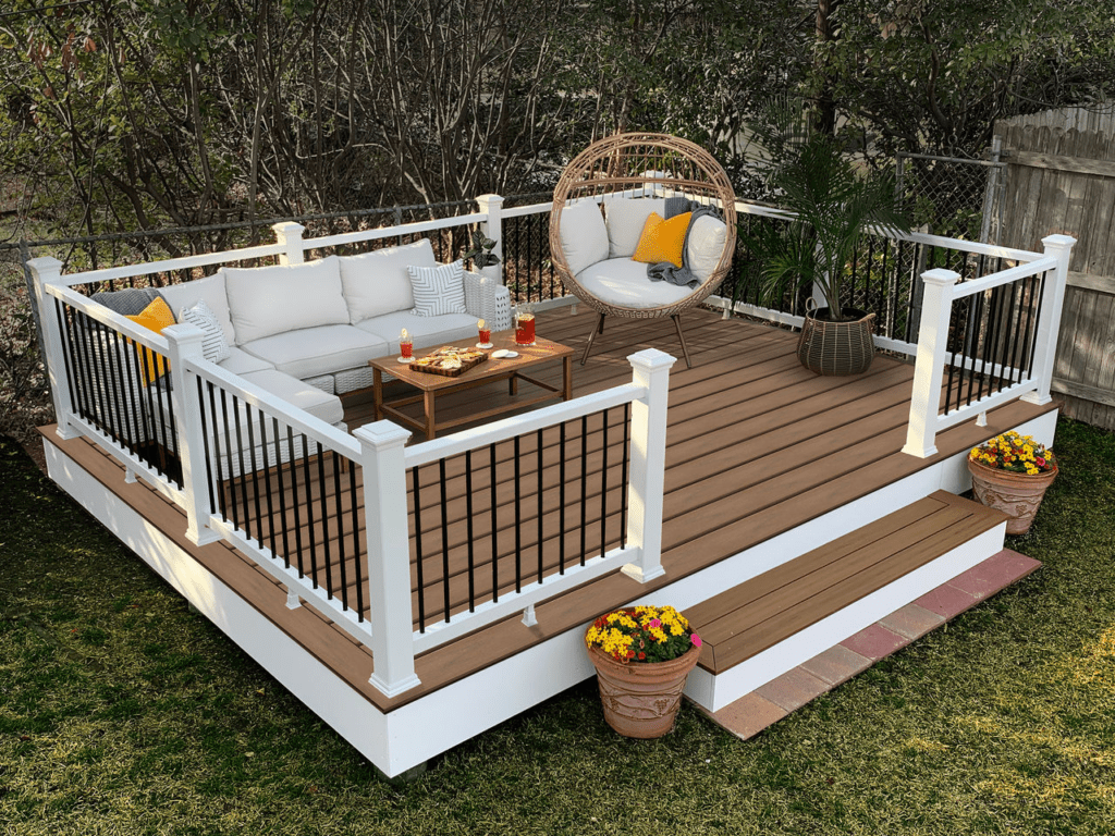 Stand-alone Trex deck with soft brown flooring, white railings, and black rod infill, elevated with a long step up from the yard.