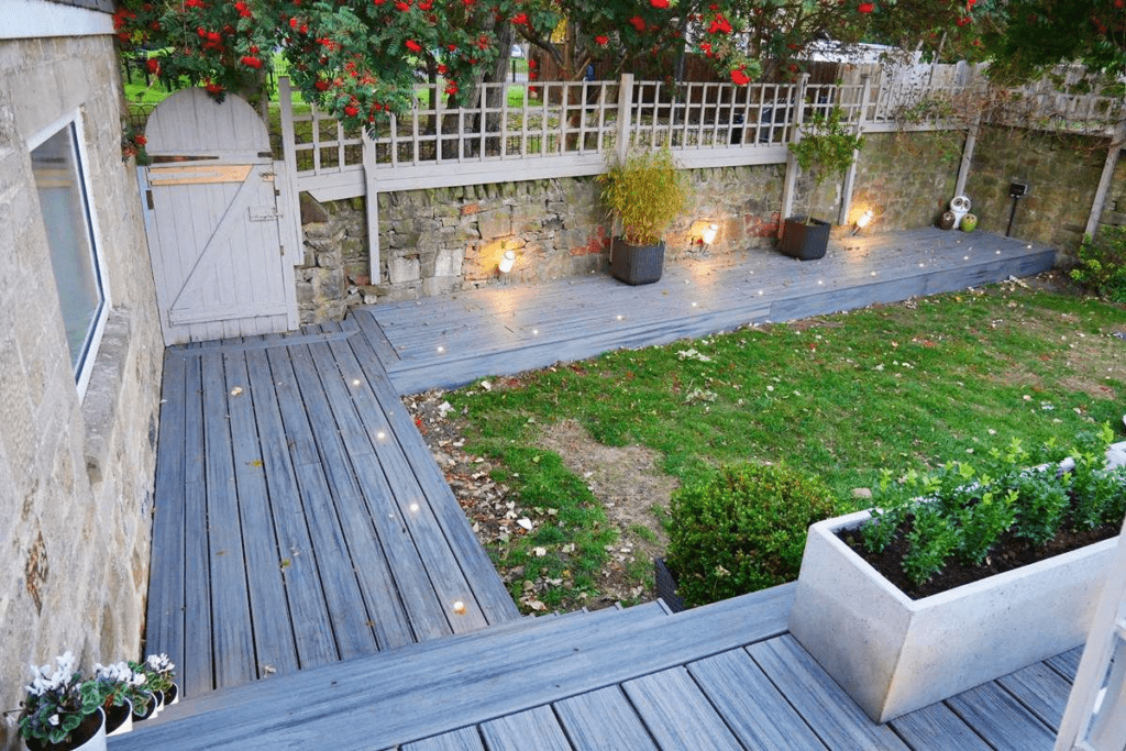 Multi-level gray Trex deck with a lower level flush to the ground and integrated lighting in the beams for a seamless, modern look.