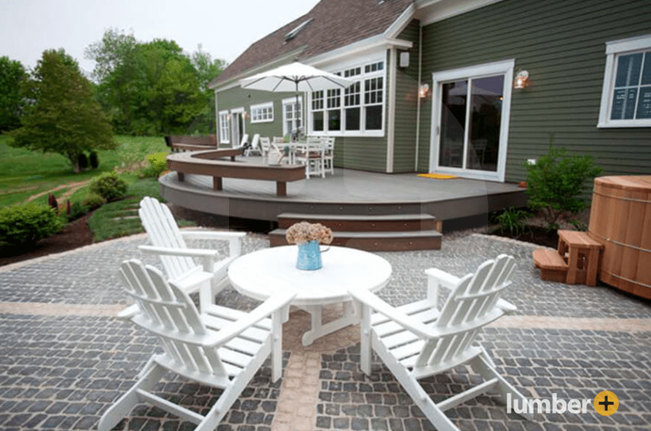 Elevated deck with a curve design on a back patio surrounded by brick sitting area.