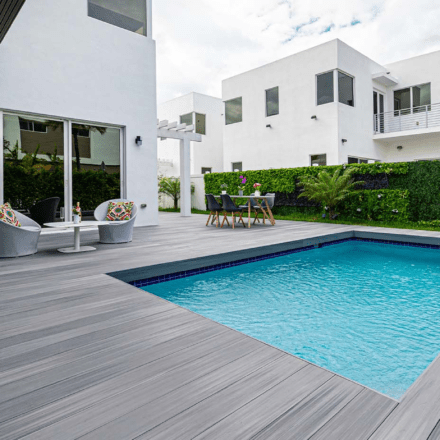 Light-gray composite decking surrounding a pool in the backyard of a modern house