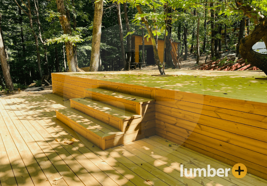 The solid foundation of a light brown deck underneath the shadows of trees.