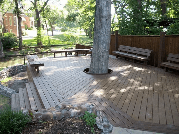 Two-toned deck with light and dark brown wood tones, built-in bench, and tree well cutout, combining style and functionality.