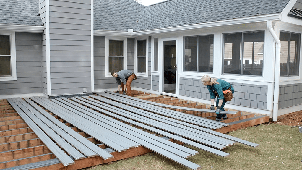 Two workers lay out Trex composite decking for installation behind the house.