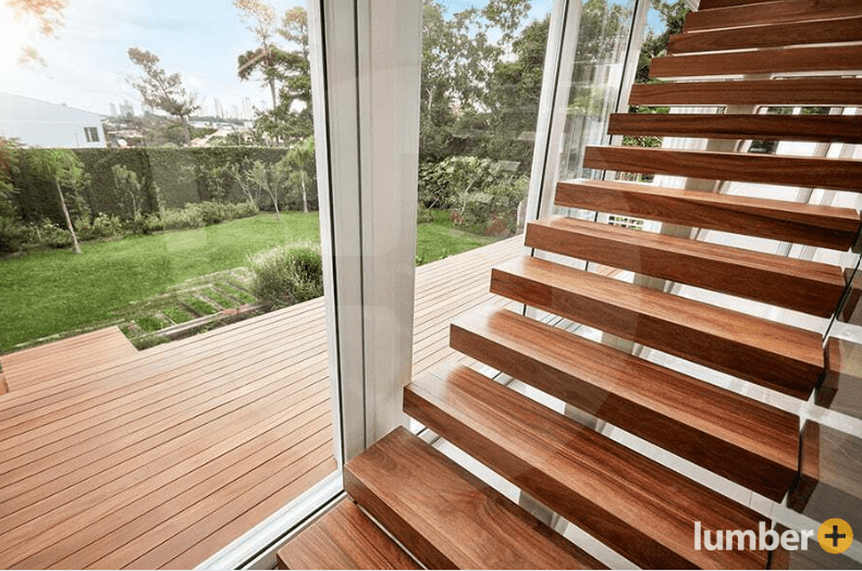 An image of floating Cumaru wood stairs beside a large window overlooking a backyard deck