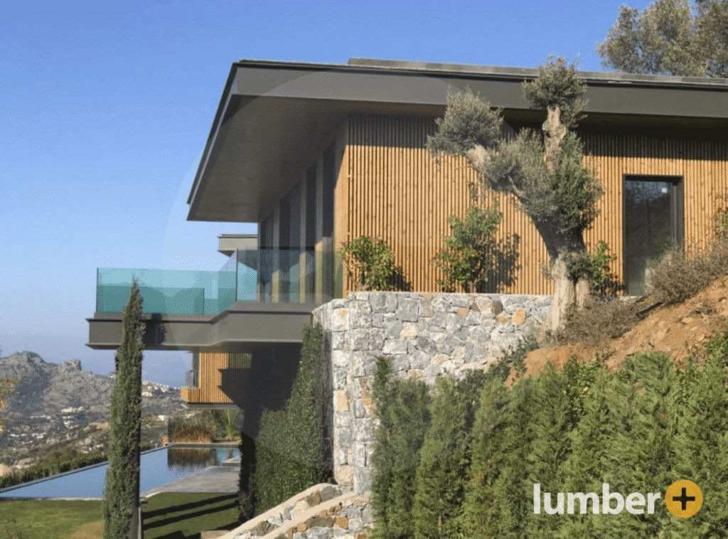 An image of a hillside modern home with vertical wood slat siding and stone retaining walls.