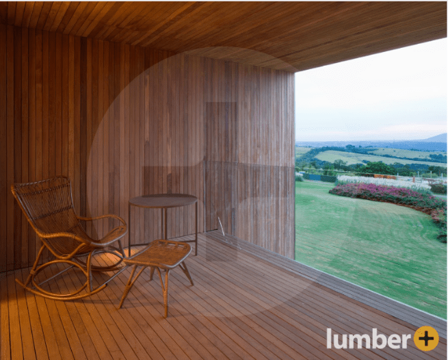 An image of a cozy wood-clad balcony with a chair, table, and open view of a grassy landscape.